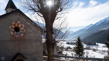 Igreja com uma janela redonda de vitrais, um campanário e vista para montanhas cobertas de neve e um vale.