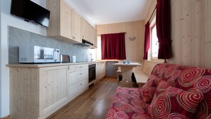 Cocina compacta con microondas, tostadora y lavabo. Se observa un banco de madera y un sofá rojo con estampado.