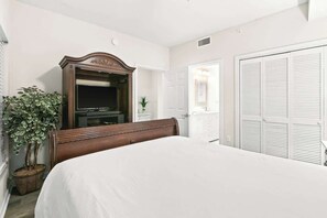 Une chambre à coucher avec un grand lit, une commode en bois, un miroir, une plante en pot et une armoire blanche.