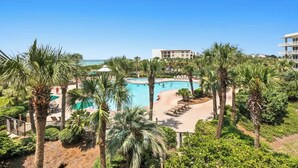 A resort with a swimming pool surrounded by palm trees, a beach area, and a view of the ocean. - The Crescent 207 (Destin)