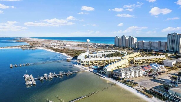 Luftaufnahme eines Küstenresorts mit einer Marina, Strandgebäuden und einem markanten Turm.