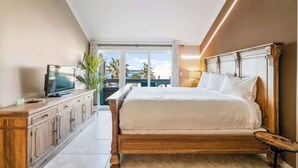 Ein Schlafzimmer mit einem hölzernen Bett, einem Fernseher auf einem Schrank und Blick ins Freie.