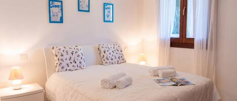 Una cama bien hecha con toallas enrolladas, una lámpara de noche y cuadros en la pared.