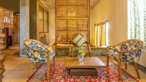A traditional room with a wooden partition, two floral-patterned chairs, a wooden table, and a red patterned rug.