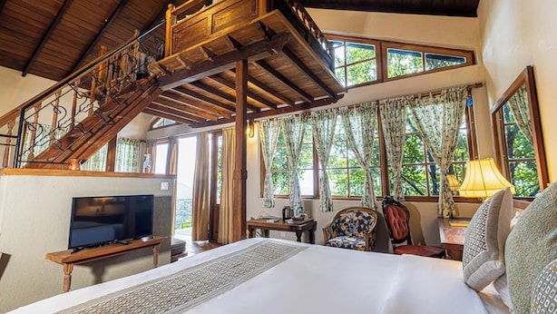A bedroom with a large bed, a TV, a desk, and a chair. There is a staircase leading to an upper level.