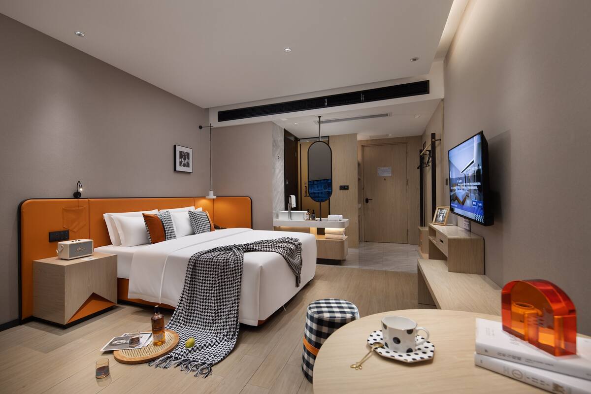 A modern hotel room with a bed, bedside tables, a TV, and a desk with a chair.