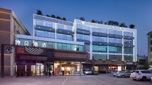 A hotel with a modern facade, multiple floors, and a parking lot in front. - SPEY HOTEL (Guangzhou)