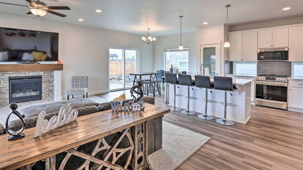 A modern kitchen with a bar area, a fireplace, and a dining space with a wooden table and bar stools. - New house in Redmond, 15 minutes to Airport and Smith Rock (Redmond)
