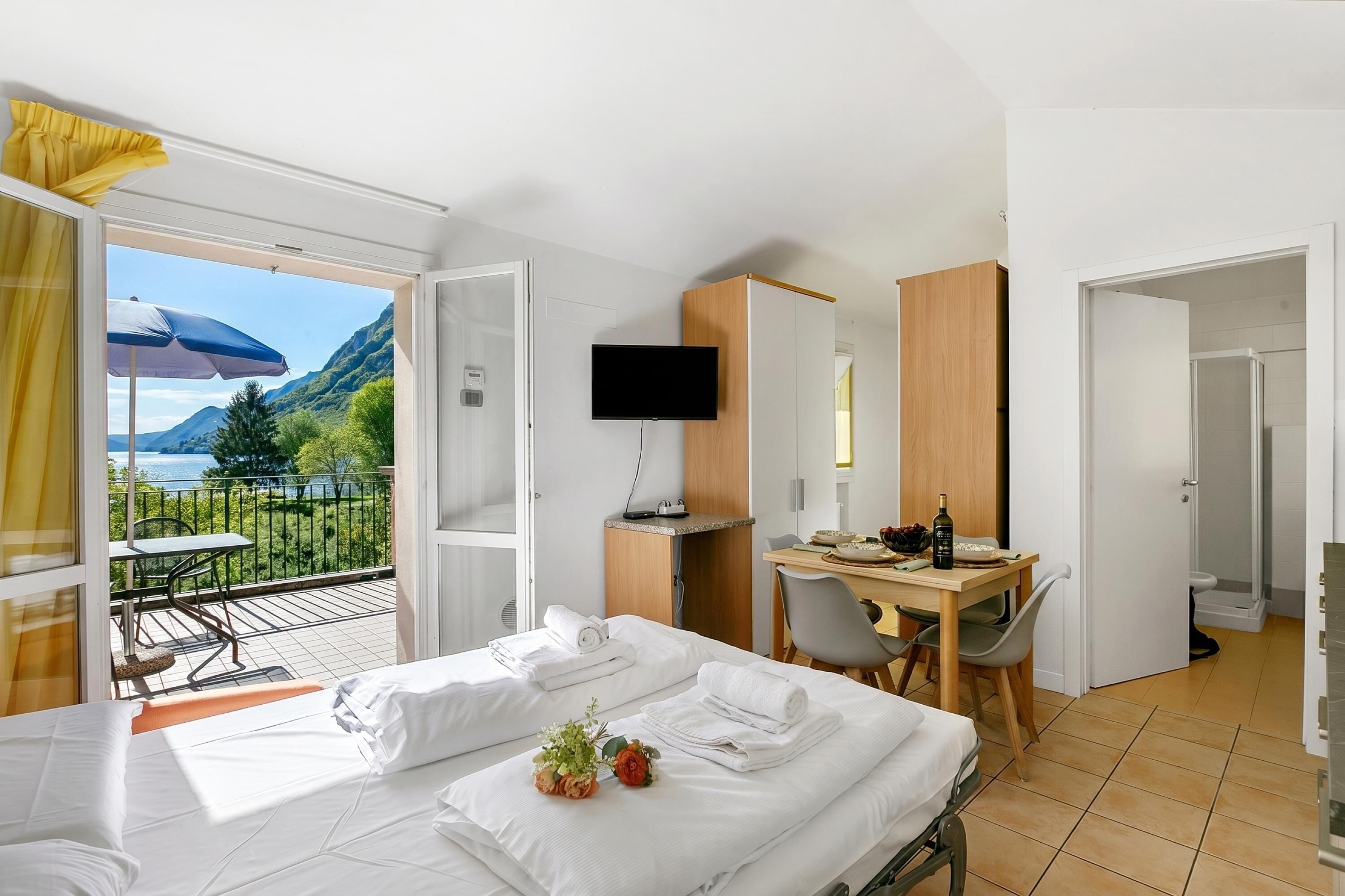 A hotel room with a bed, a desk, a TV, and a balcony with a table and chairs.
