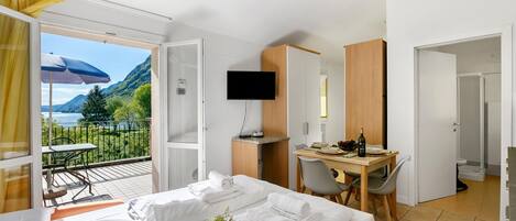 A hotel room with a bed, a desk, a TV, and a balcony with a table and chairs.
