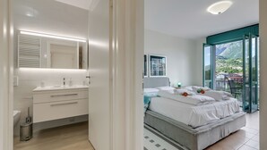 Une chambre moderne avec un grand lit, une salle de bain avec un meuble-lavabo et un balcon offrant une vue sur les montagnes.