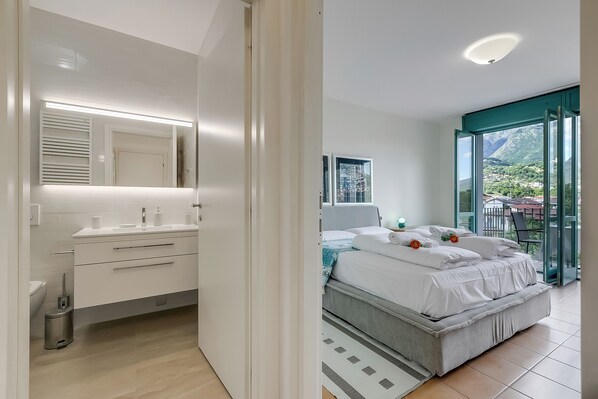 Et moderne soveværelse med en stor seng, et badeværelse med et toiletbord, og en balkon med udsigt til bjergene.