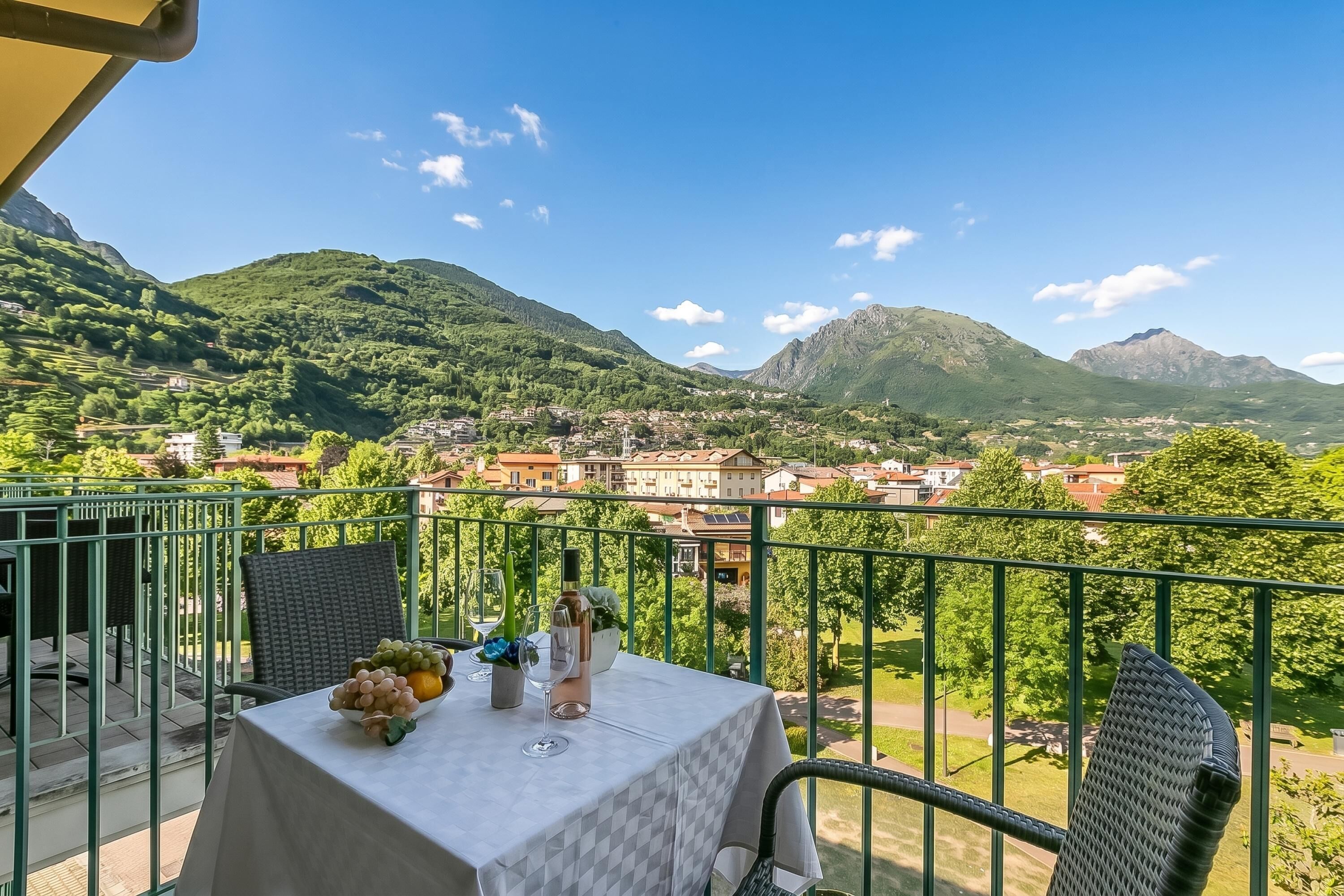 A balcony with a table set for two, overlooking a mountainous landscape with a village below.