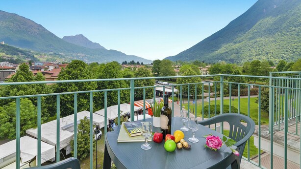 Een balkon met een eettafel, met uitzicht op een bergachtig landschap en een dorpje beneden.