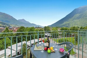 A balcony with a table set for dining, overlooking a mountainous landscape with a view of a village below. - (Porlezza)