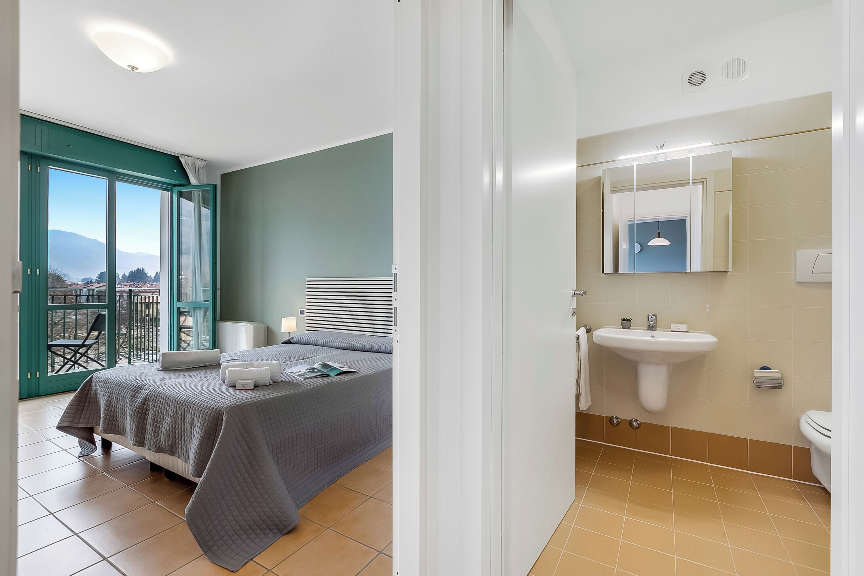 A bedroom with a bed, a window with a view, a bathroom with a sink and toilet.