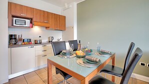 Een moderne keuken met houten kastjes, een magnetron en een eettafel gedekt voor vier personen met stoelen.