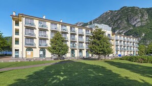 Een hotel met meerdere verdiepingen, balkons, een gazon en een berg op de achtergrond.