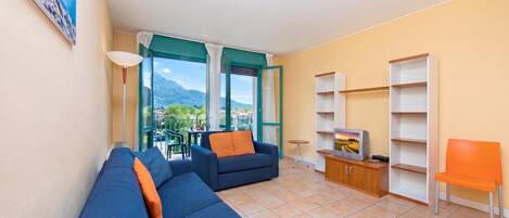 A living room with a sofa, a TV stand, and a view of mountains through a glass door.