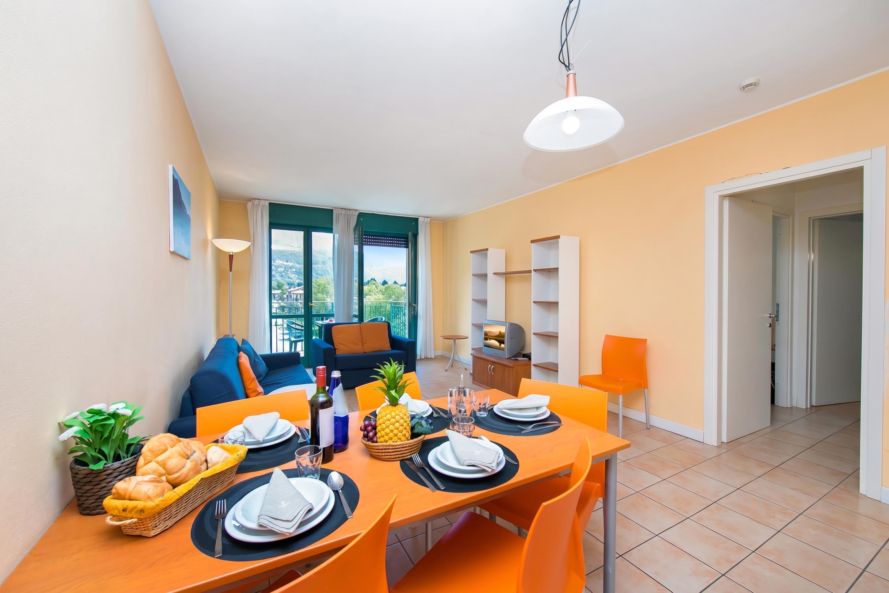 A dining area with a table set for two, a sofa, and a TV in the background.