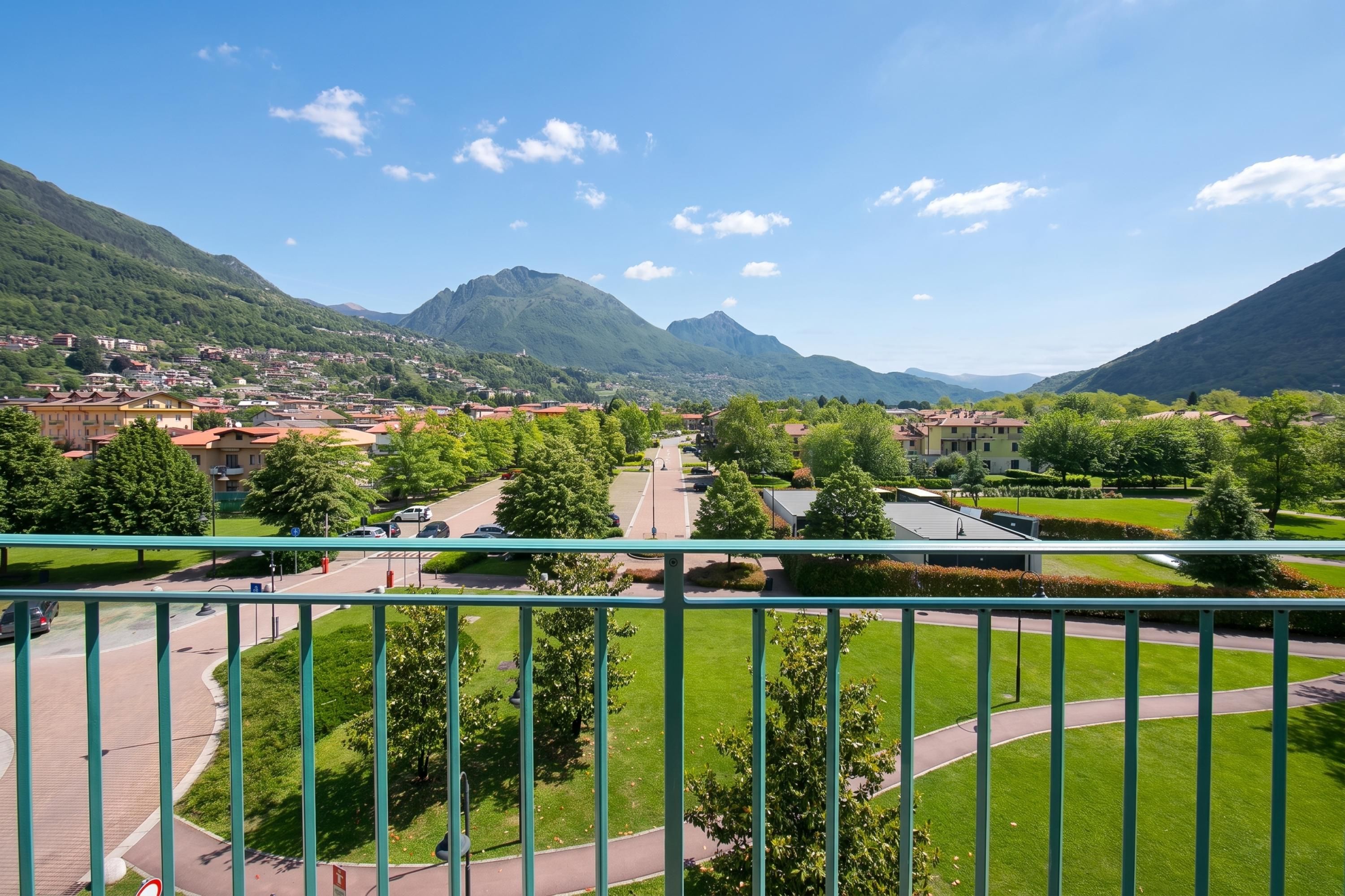 A town with a mountain backdrop, featuring a paved road, green spaces, and residential buildings.