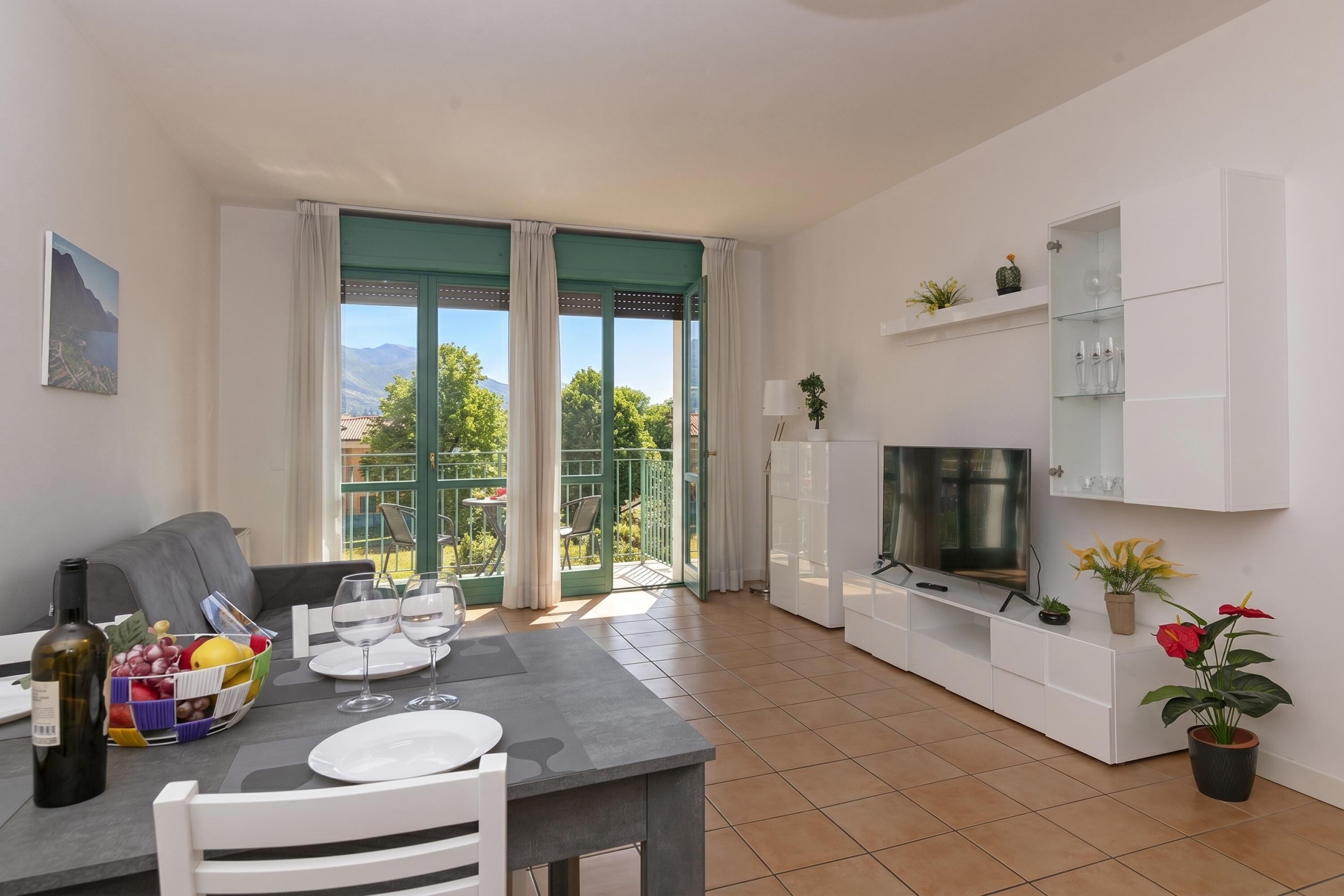 A modern living room with a dining area, a TV, and a balcony with a view.