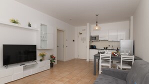 En moderne stue med et fladskærms-tv, en grå sofa og et spiseområde med et bord og stole.