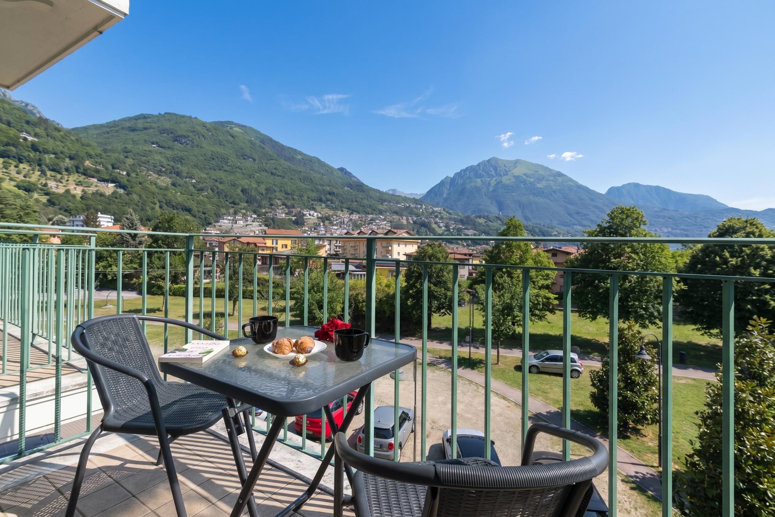 A balcony with a table, chairs, and a view of a town and mountains.