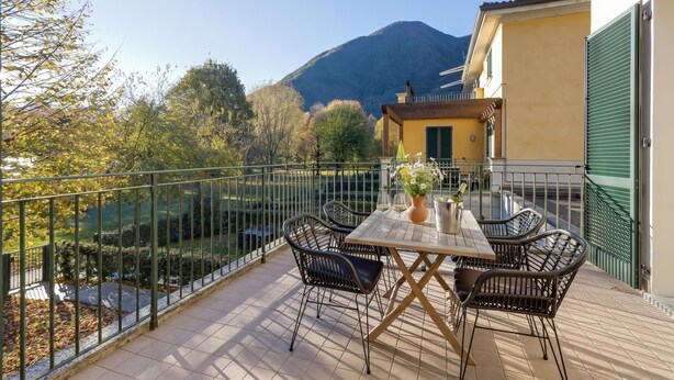 Un balcon avec une table et des chaises, une vue sur une montagne et une clôture verte.