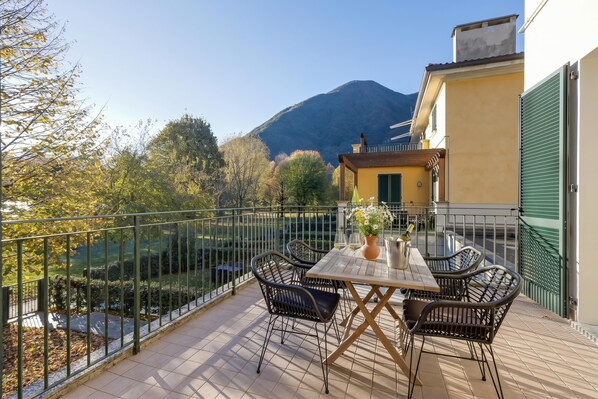 A balcony with a table and chairs, a view of a mountain, and a green fence.