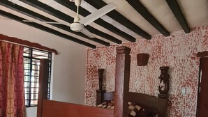 A bedroom with a wooden bed, a patterned rug, a ceiling fan, and a window with bars. - Charming 2-bed Cottage in Bodo, a Fishing Village (Shirazi)