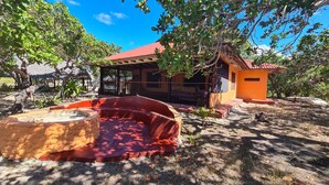 A rustic outdoor area with a stone seating area, a wooden structure with a red roof, and a small orange building. - Charming 2-bed Cottage in Bodo, a Fishing Village (Shirazi)
