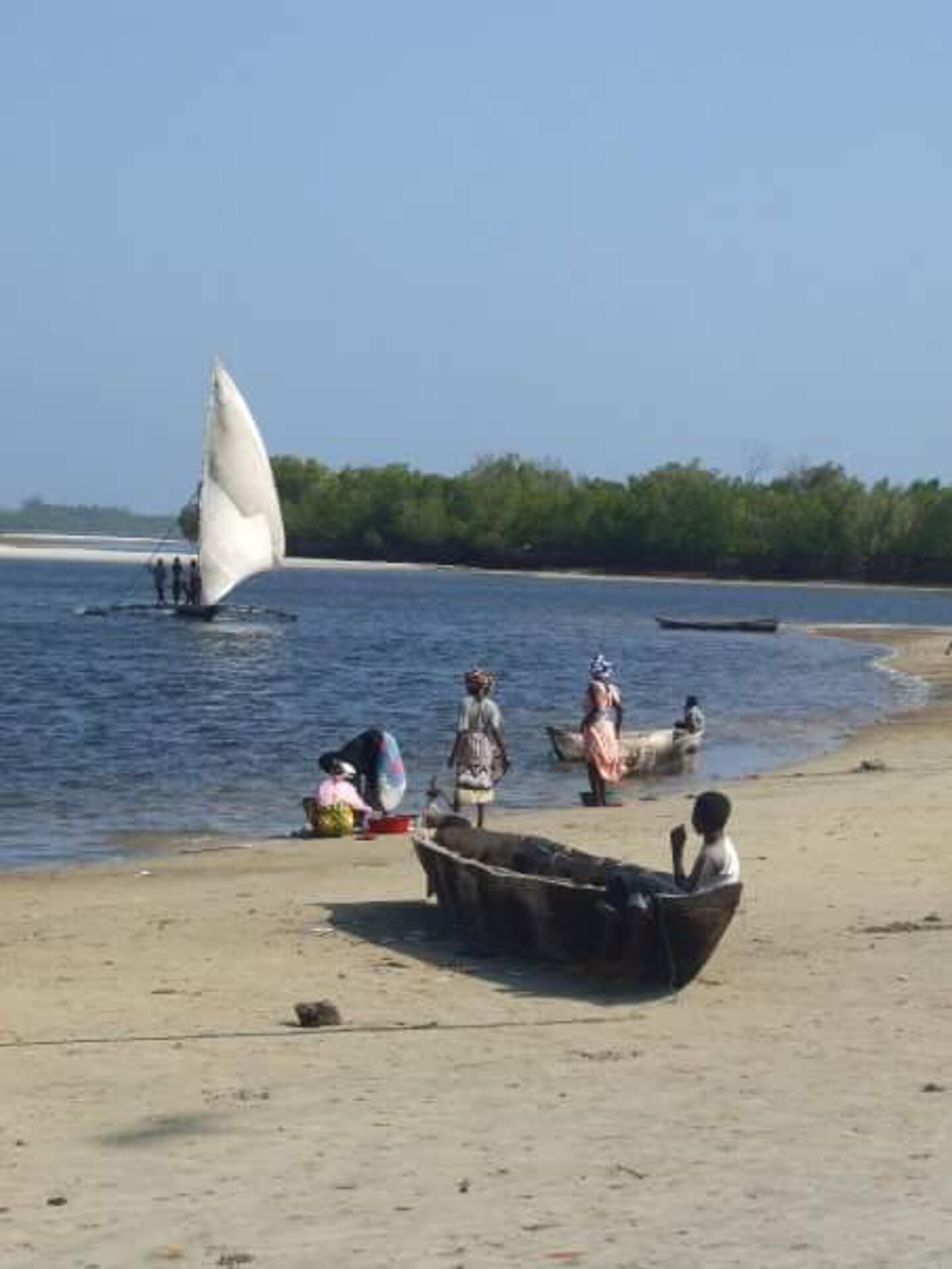 A beach scene with a sailboat, people, and a small boat on the shore.
