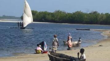 A beach scene with a sailboat, people, and a small boat on the shore.