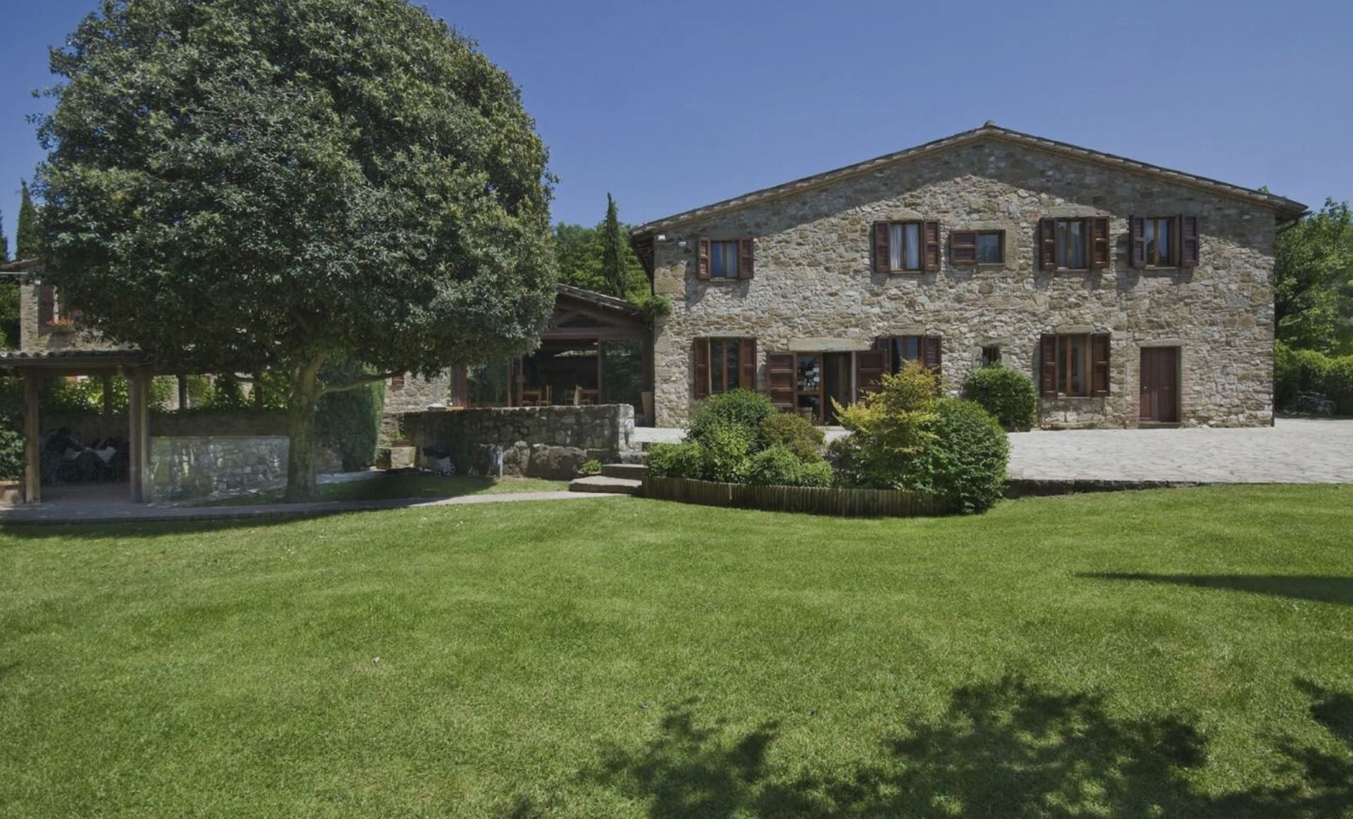 A stone building with a well-maintained lawn and a large tree in the foreground.