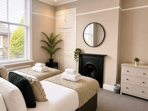 Une chambre avec deux lits, une cheminée, un miroir et une commode.