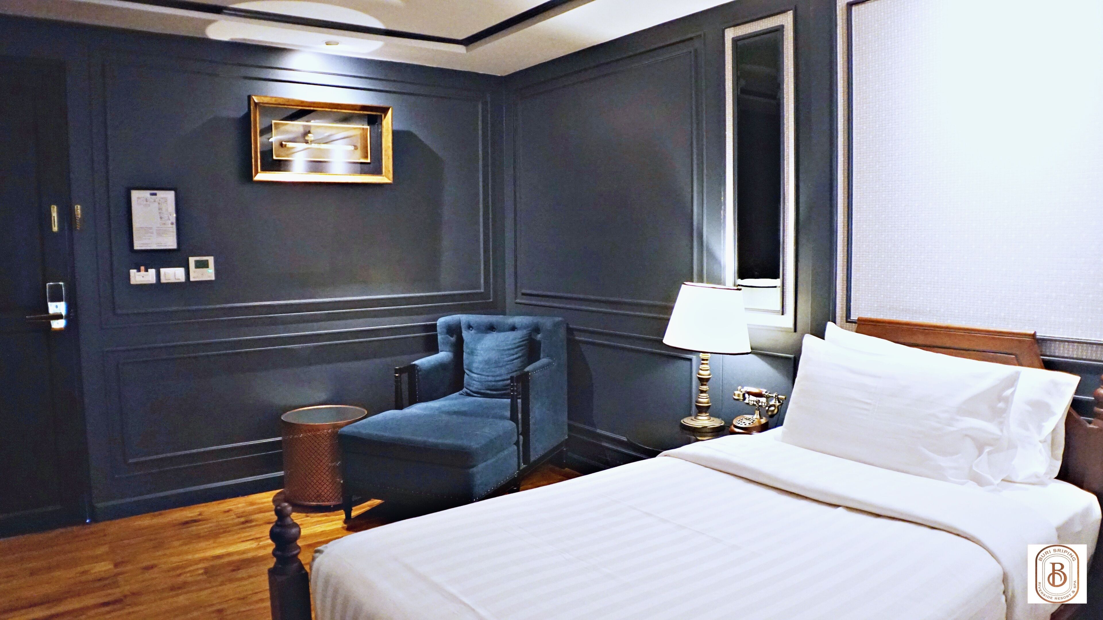A hotel room with a bed, a chair, a lamp, a telephone, and a wall-mounted picture.