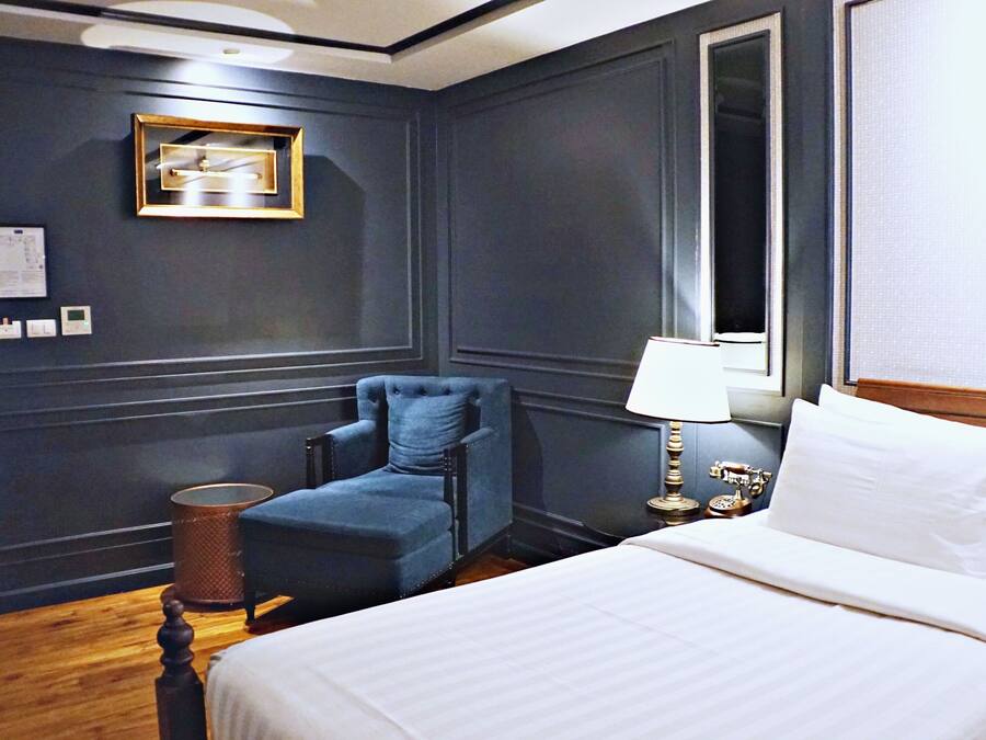 A hotel room with a bed, a chair, a lamp, a telephone, and a wall-mounted picture.