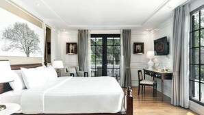 Ein Hotelzimmer mit einem großen Bett, einem Schreibtisch, einem Stuhl und Blick auf Bäume durch ein Fenster.