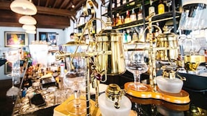 Eine Bar mit verschiedenen goldfarbenen Bartools und Gläsern, Regalen mit Flaschen und einer Holzzielung.