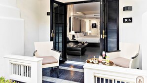 Ein Hotelzimmer mit einem Bett, zwei Stühlen, einem Tisch mit Getränken und Blick auf den Flur.