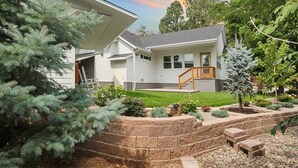 A two-story house with a front porch, a wooden staircase, and a landscaped garden with various plants and a small tree. - White Peak Lodge *Ping-Pong*Pool-Table*PACMAN* (Flagstaff)