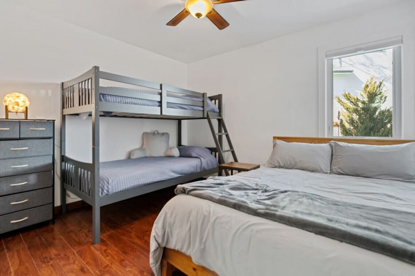 A bunk bed room with a dresser, a ladder, and a window with a view of trees.