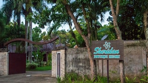 A sign for Sheridan Boutique Resort with a gated entrance and lush greenery.