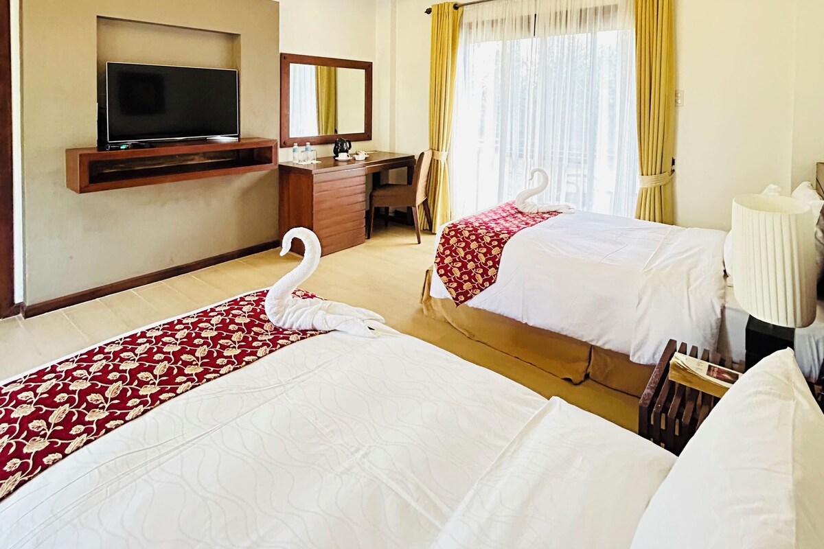 Habitación de hotel con dos camas, televisión, escritorio y ventana con cortinas.