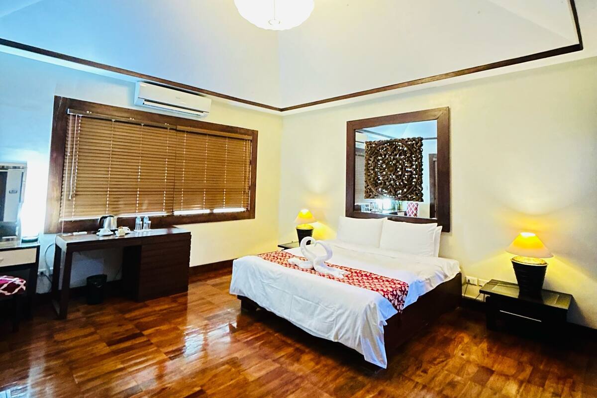 A bedroom with a bed, bedside lamps, a desk, and a large window with blinds.