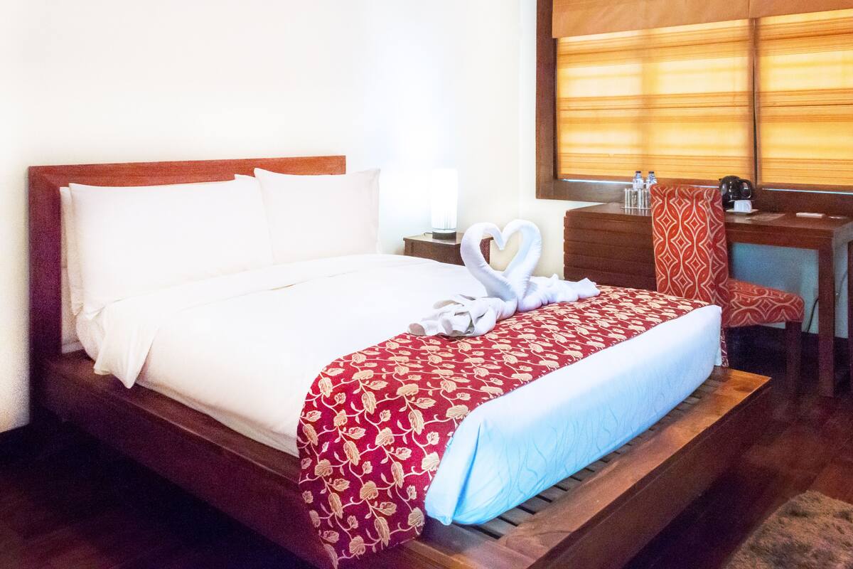 A neatly made bed with a red and white patterned bedspread, a white pillow, and a heart-shaped towel on the side.