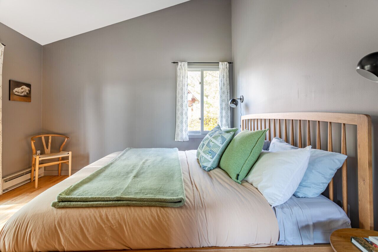 Een slaapkamer met een bed, een stoel, een raam met gordijnen en een lamp.