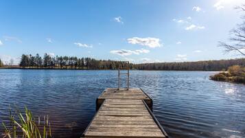 A wooden dock extending into calm water with a clear sky and trees in the background.