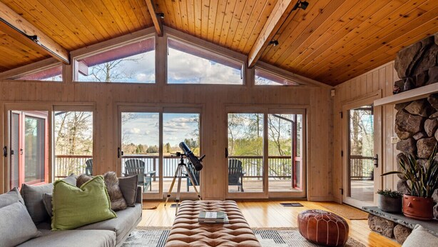 A spacious living room with a high ceiling, large windows, a sofa, a bench, and a telescope.